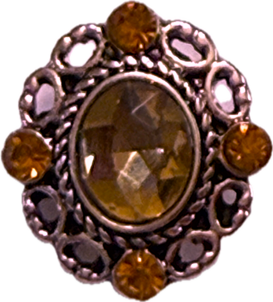 A snap charm with an oval rhinestone in the center and filigree edge, surrounded by smaller orange rhinestones.